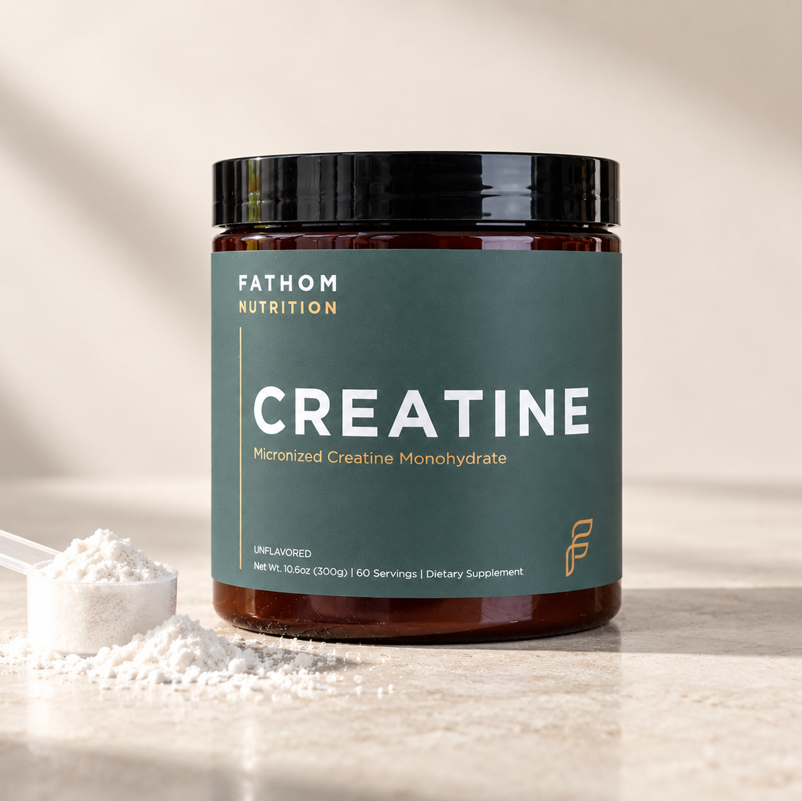 A jar of Fathom Nutrition Creatine Micronized Creatine Monohydrate with a dark green label and black lid, shown on a light stone surface with a scoop of white powder beside it.