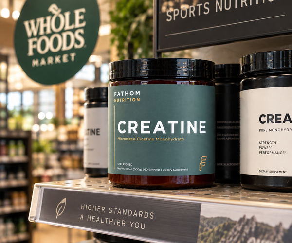 A jar of Fathom Nutrition Creatine Monohydrate displayed on a store shelf, with other supplement containers and a Whole Foods Market sign in the background.
