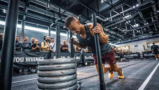 Person lifting weights in a gym setting with spectators and banners in the background